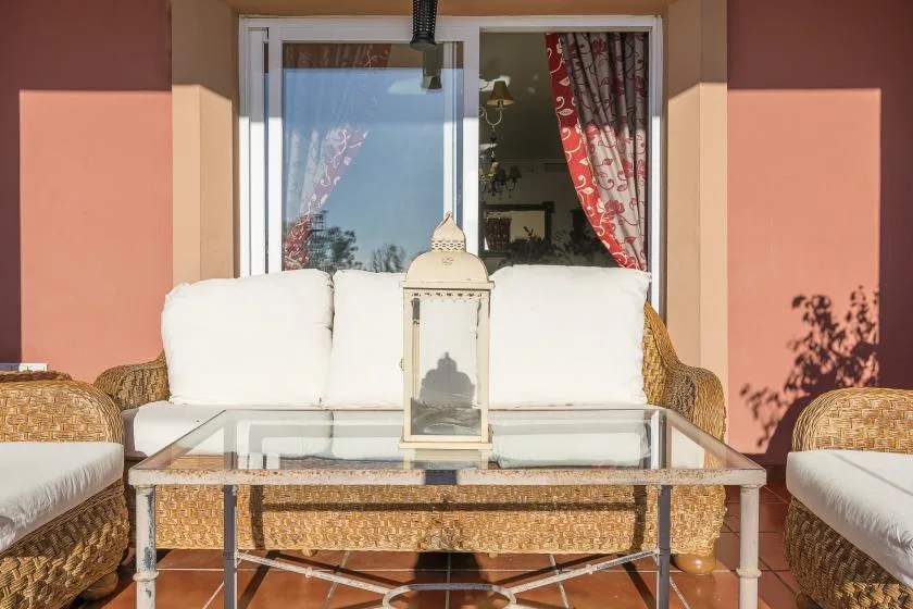 A patio seating area with a glass-topped table in front of a curtained window.