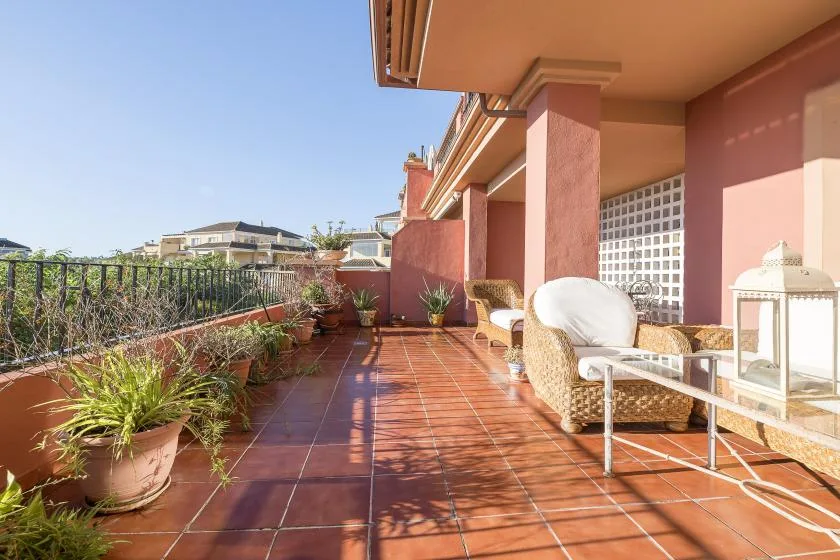 A sunlit terrace with tiled flooring, potted plants, and outdoor seating.