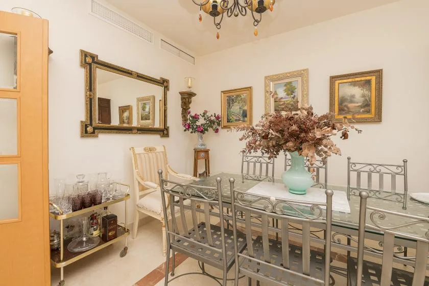 A dining room with a glass-topped table, metal seating, and framed artwork.