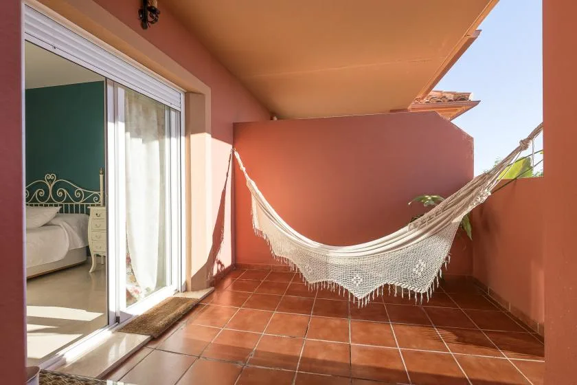 A tiled balcony with a hammock beside an open sliding glass door.