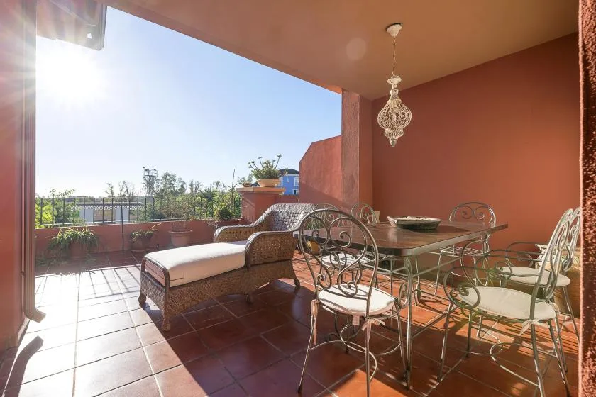 A sunlit terrace with a cushioned lounge seat and outdoor dining table.