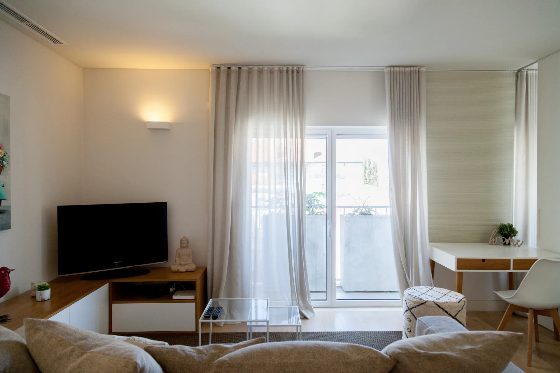 Una sala de estar luminosa con asientos, un televisor y puertas de vidrio que dan a un balcón.