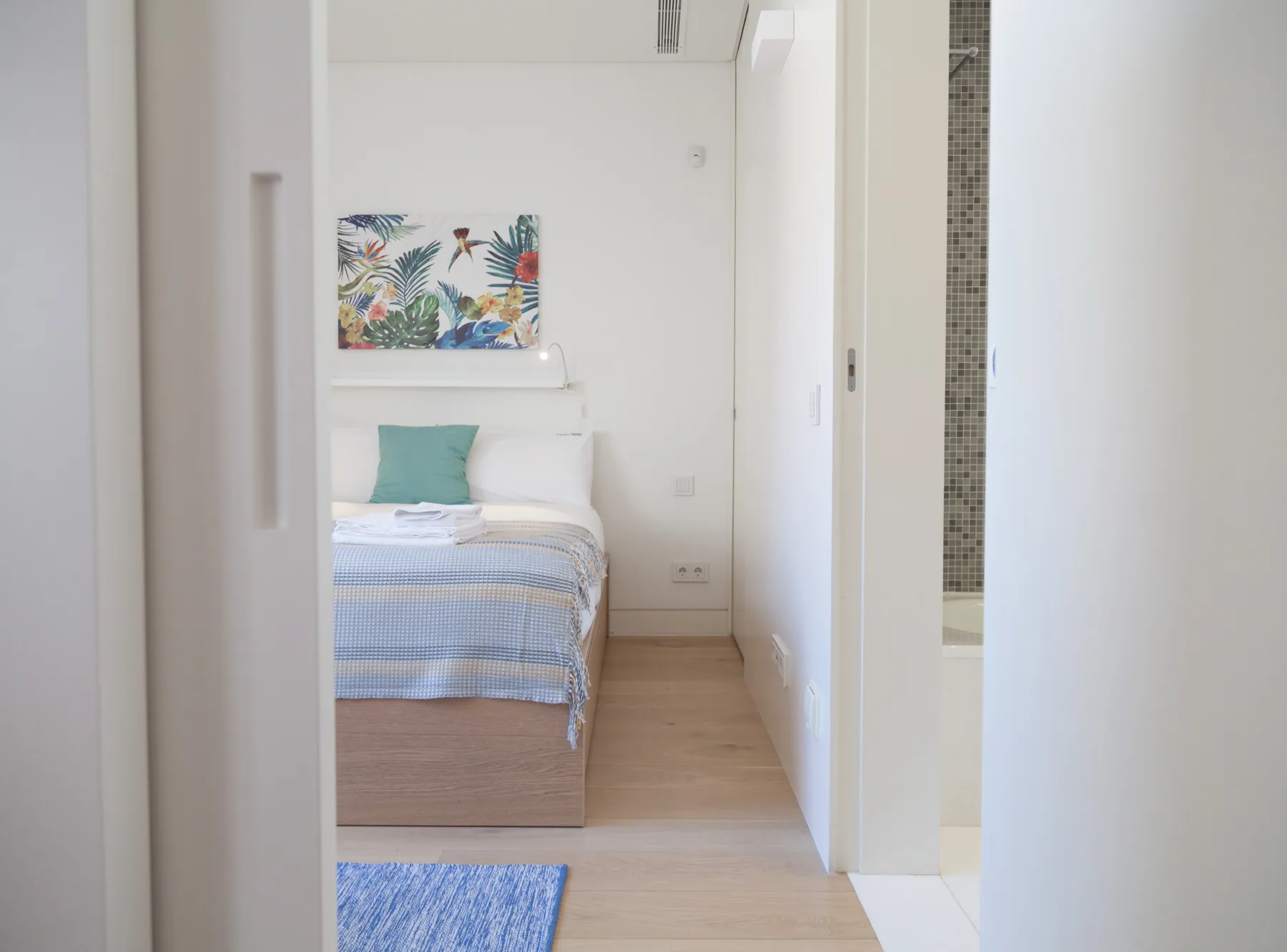 Dormitorio con una cama bien tendida y una obra colorida encima.