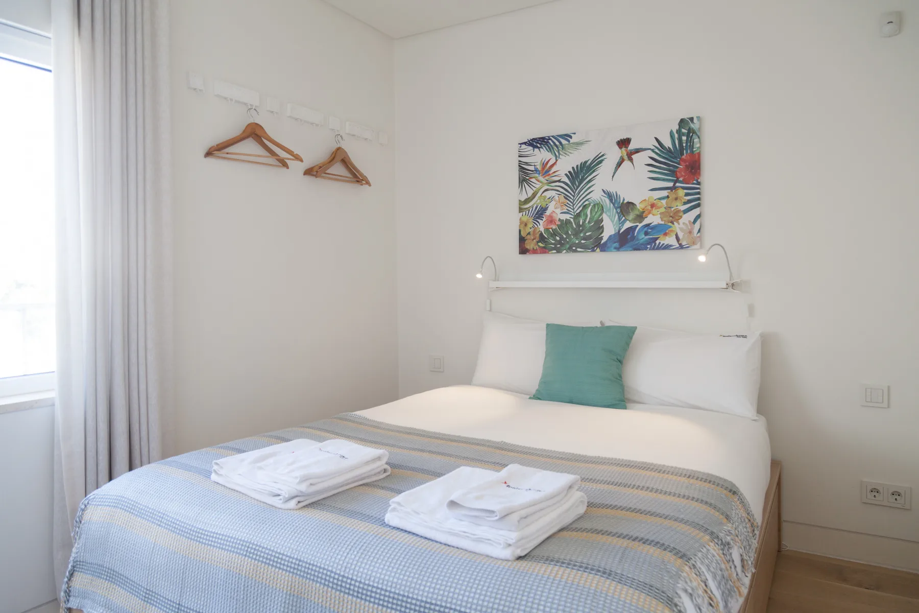 Un dormitorio con una cama bien hecha y una colorida obra de arte sobre el cabecero.
