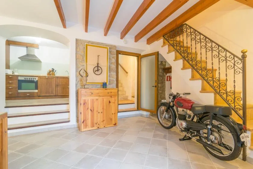 A tiled interior with a wooden staircase, kitchen area, and parked motorcycle.