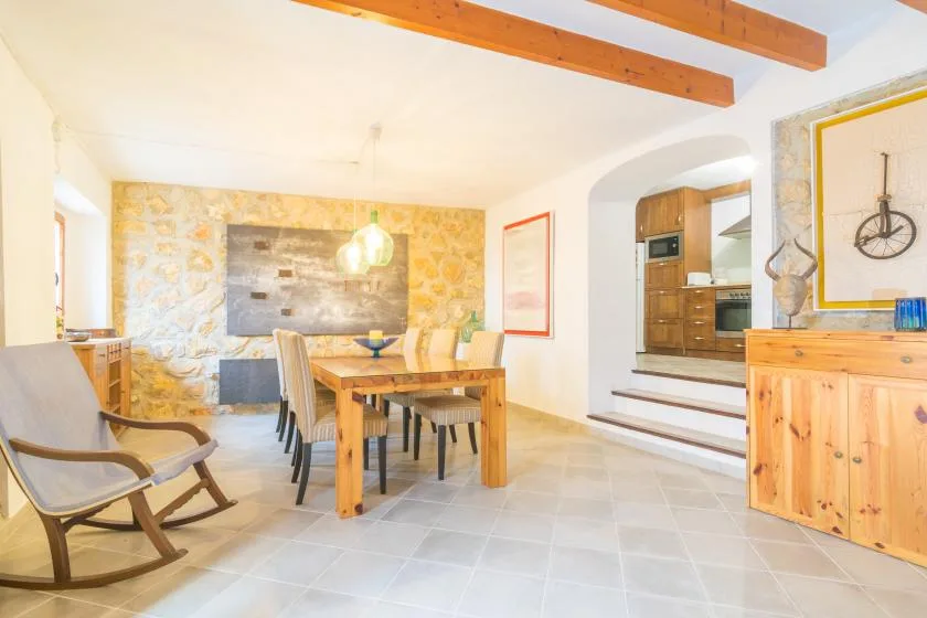 A bright dining area with a wooden table and seating beside an open kitchen.