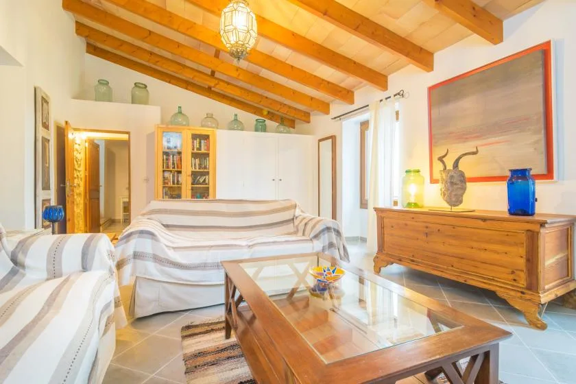 A bright living room with striped seating, a glass coffee table, and exposed wooden ceiling beams.
