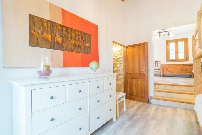 A bright bedroom with a white dresser and a wooden bed in the adjoining area.