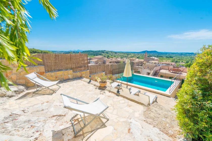 A sunlit outdoor terrace overlooks a swimming pool and distant countryside.