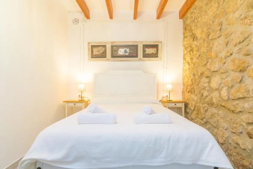 A bright bedroom with a neatly made bed and exposed ceiling beams.