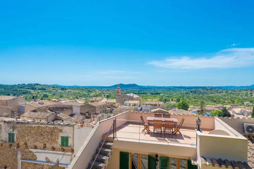 Rooftop terrace overlooking a town, with outdoor seating and distant hills.