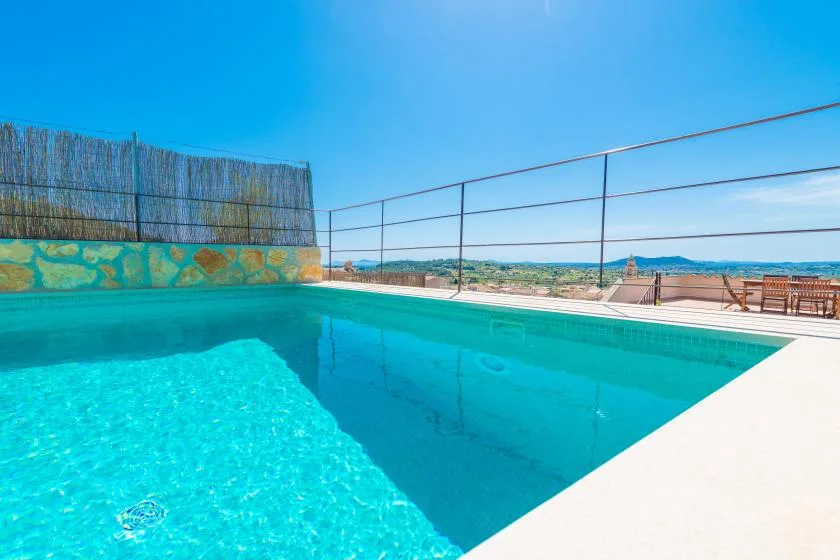 An outdoor swimming pool overlooks the distant landscape beneath a clear blue sky.
