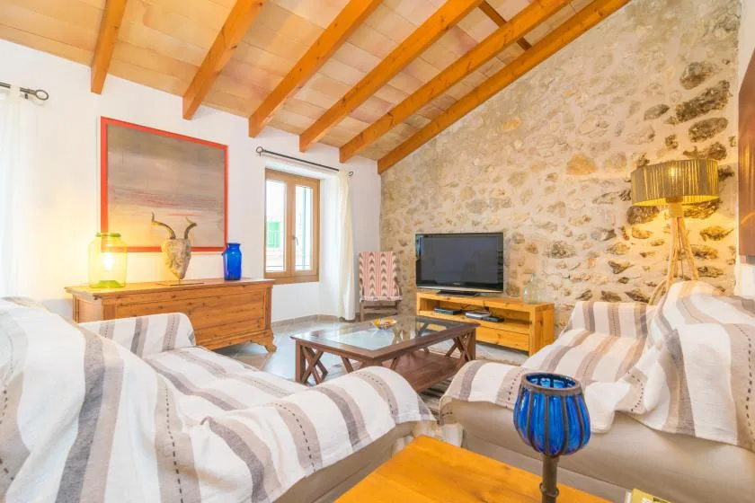 A bright living room with striped seating, a television, and exposed ceiling beams.