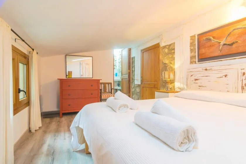A bright bedroom with white bedding, a wooden dresser, and framed wall art.