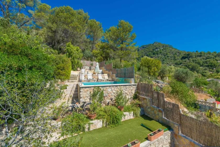 An outdoor swimming pool sits among greenery and stone walls on a sunny hillside.