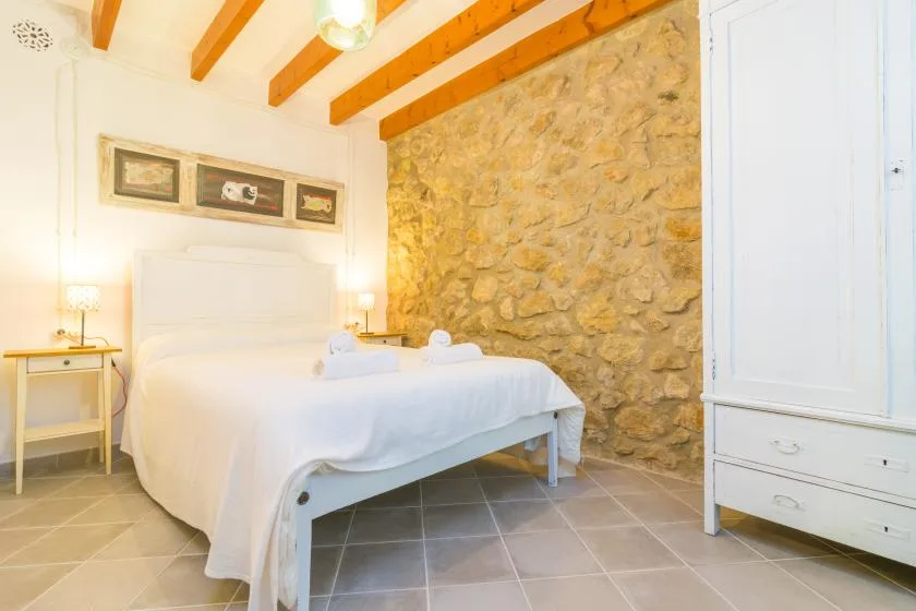 A bedroom with a white bed beside a stone wall.