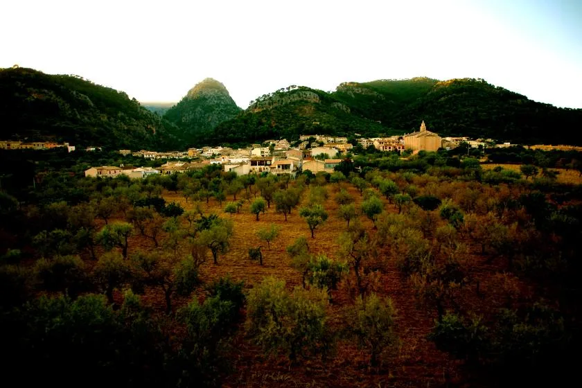 A hillside village sits among cultivated fields, with mountains rising behind it.