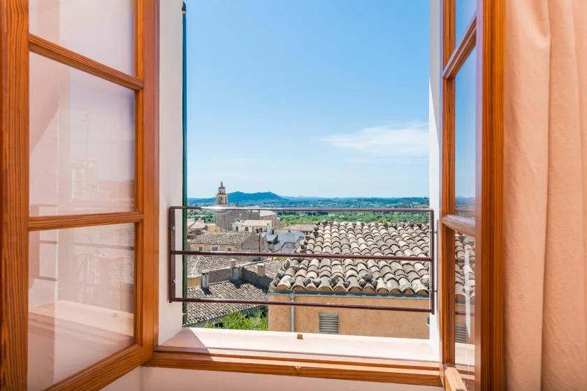 An open window frames tiled rooftops and a distant coastal view.