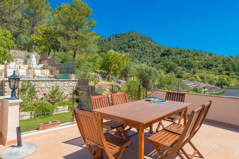An outdoor dining terrace overlooks a green hillside under a clear blue sky.
