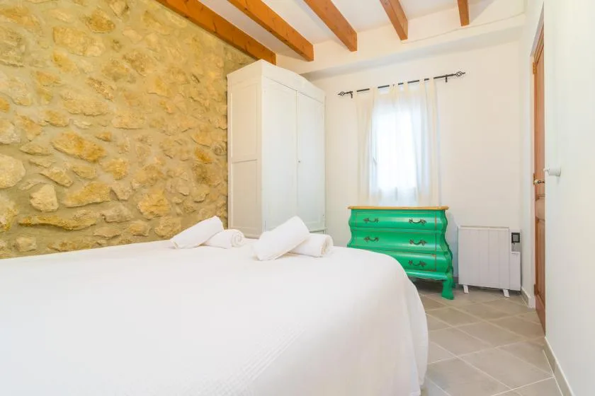 A bedroom with a white bed, a green dresser, and a stone wall.