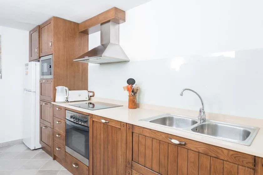A bright kitchen with wooden cabinetry, a cooktop, and a double sink.