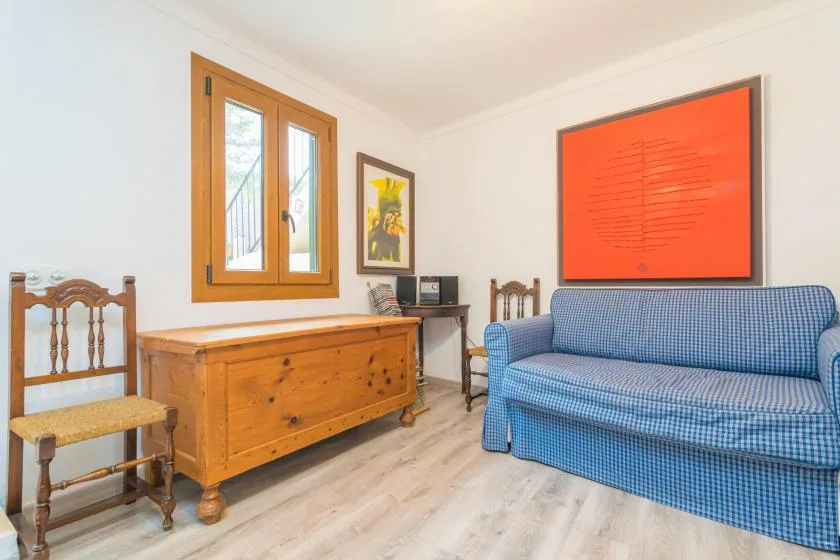 A living room with blue seating, a wooden chest, and framed artwork.