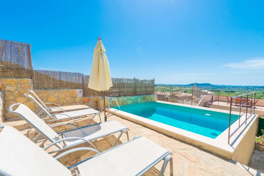 A sunny outdoor pool area with lounge chairs and a closed umbrella.
