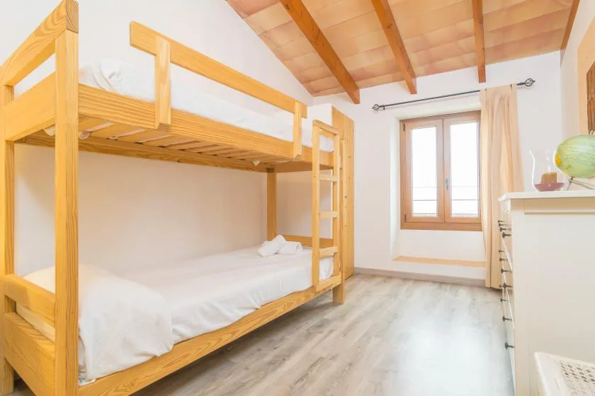 A bright bedroom with wooden bunk beds and a window.