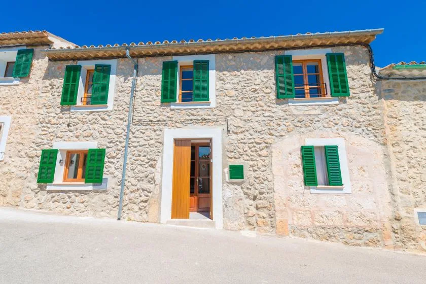 A stone building facade with green shutters and an open doorway.