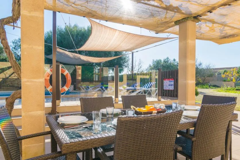 An outdoor dining area with a glass table and woven seating sits beside a pool.