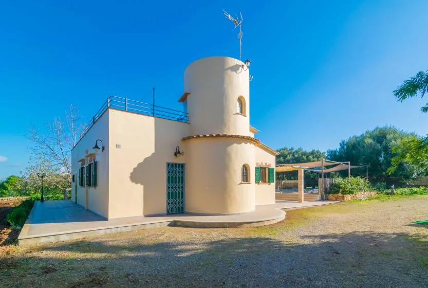 A cream-colored house with a rounded tower stands beside a gravel yard.