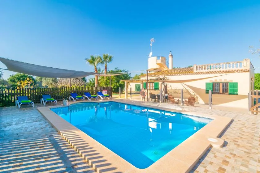An outdoor swimming pool beside a low building, with shaded seating nearby.