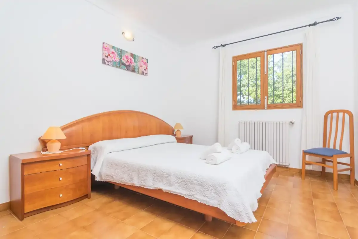 A bedroom with a neatly made bed, wooden bedside tables, and a window.
