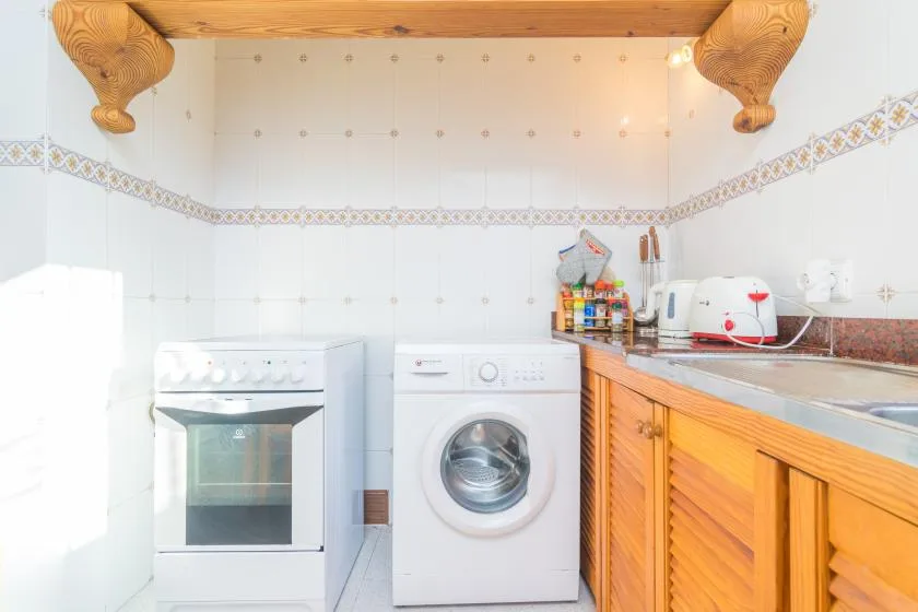A tiled utility room with a washing machine, oven, and wooden counter.
