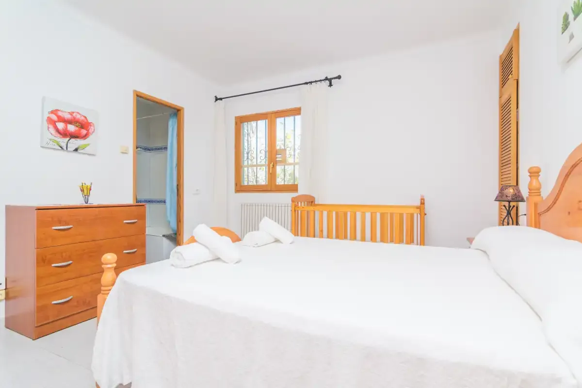 A bright bedroom with a bed, wooden dresser, and window.