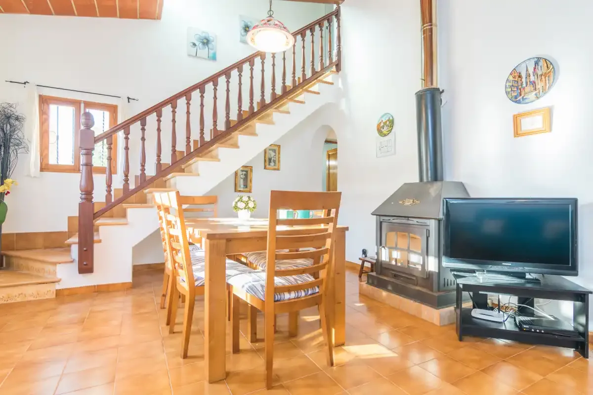 A dining area sits beneath a wooden staircase, with a fireplace and television nearby.