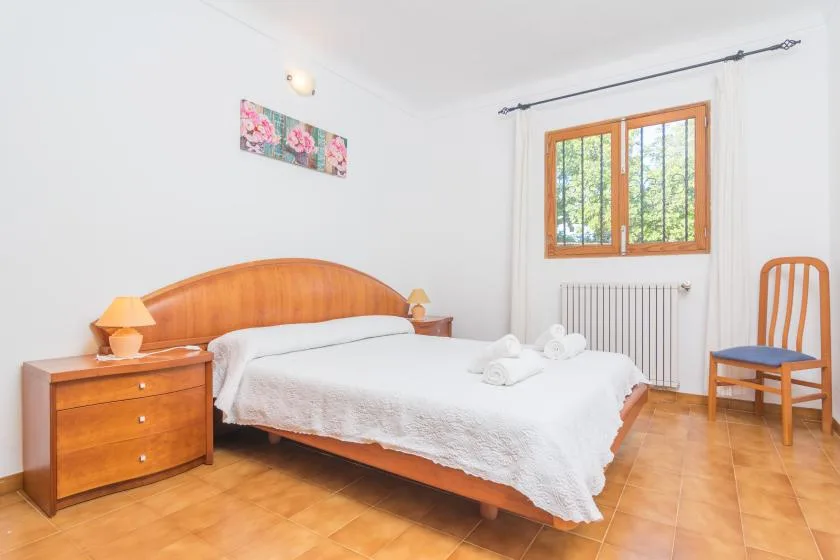 A bright bedroom with a wooden bed, white bedding, and a window.