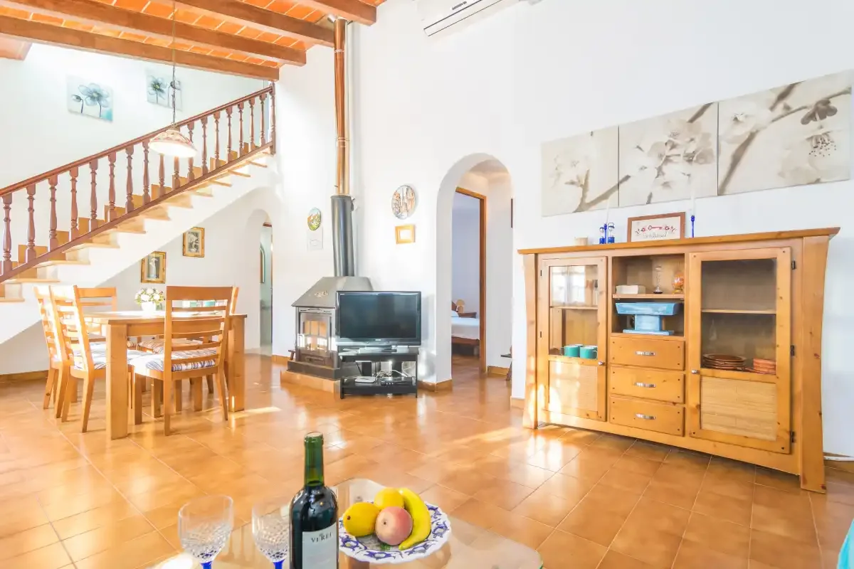 A bright living and dining area with a wooden staircase and cabinet.