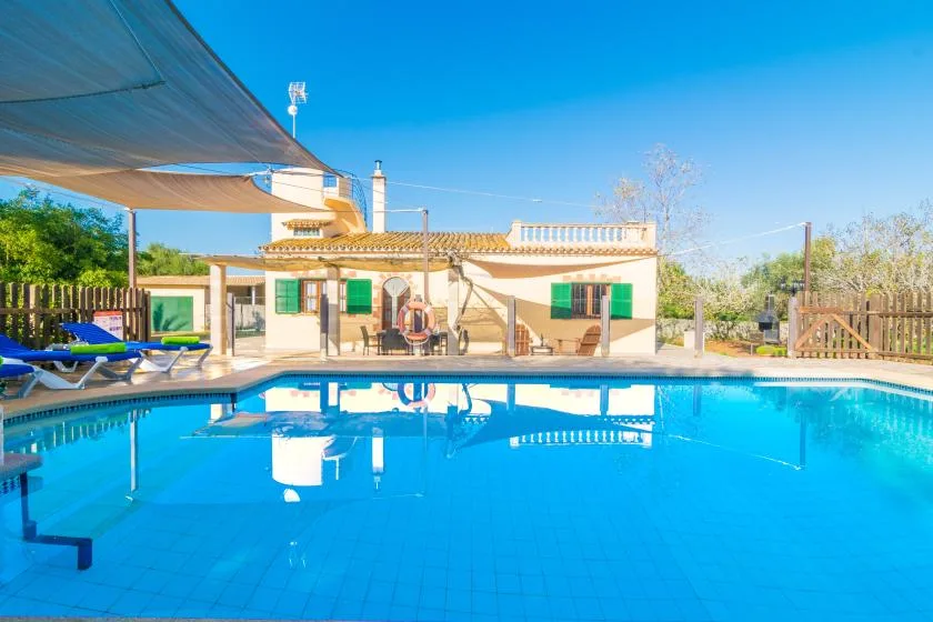 An outdoor swimming pool sits in front of a low building under a clear blue sky.