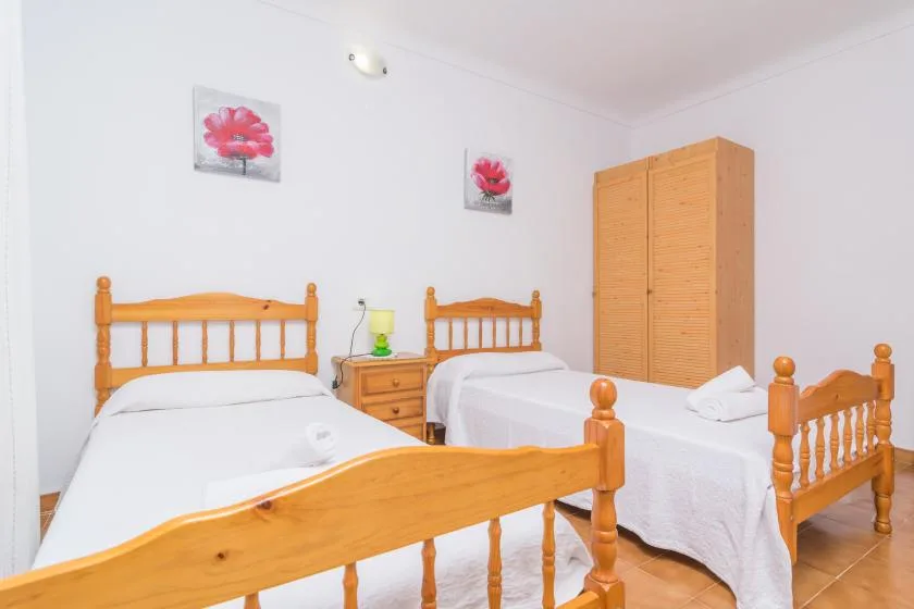 A bright bedroom has two wooden beds with white bedding and a wardrobe.