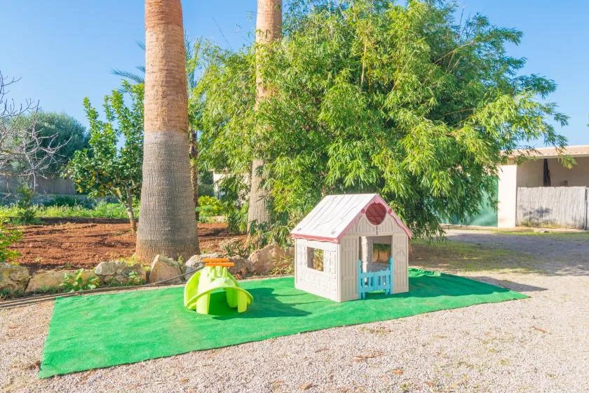 An outdoor play area with a small playhouse on green ground cover.