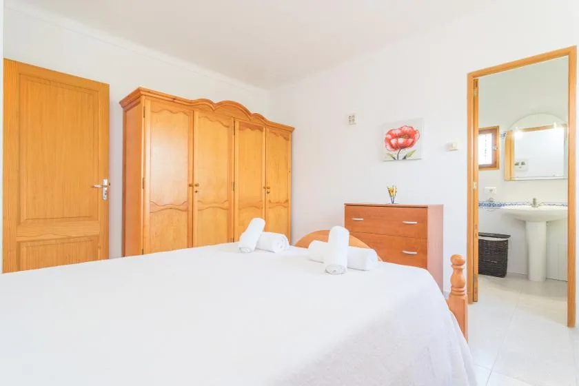A bright bedroom with a large bed, wooden wardrobe, and bathroom doorway.