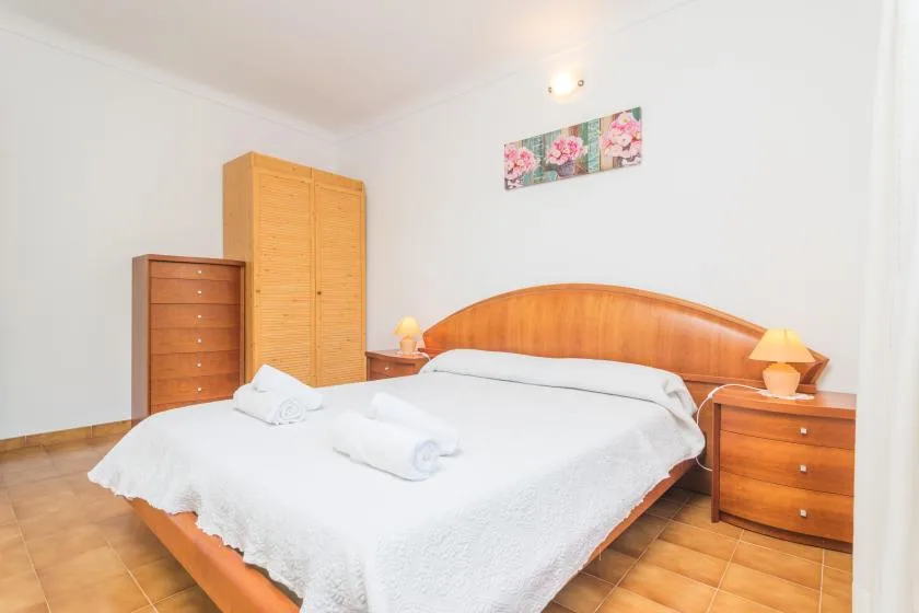 A bedroom with a wooden bed, white bedding, and matching storage furniture.