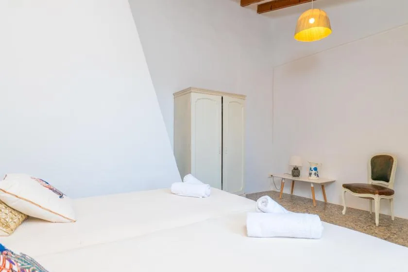 A bright bedroom with white bedding and a small table beside a chair.
