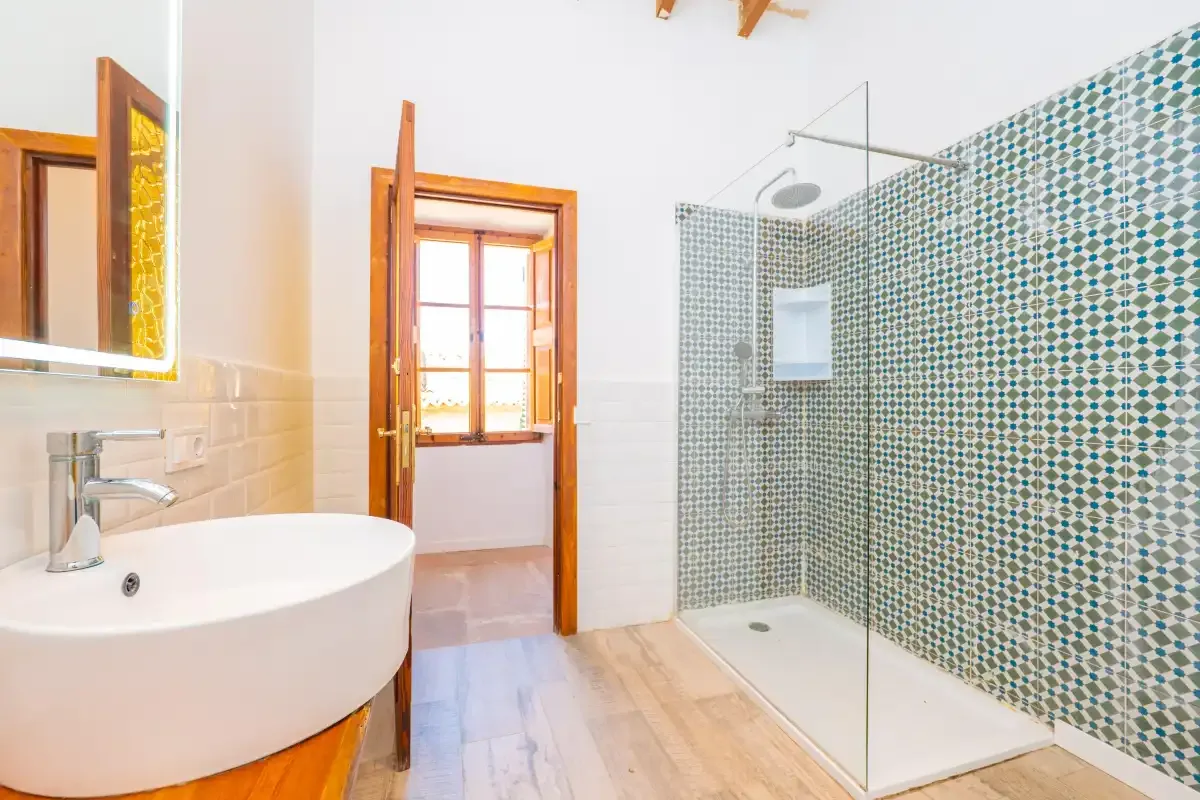A bright bathroom with a sink, walk-in shower, and wooden-framed doorway.