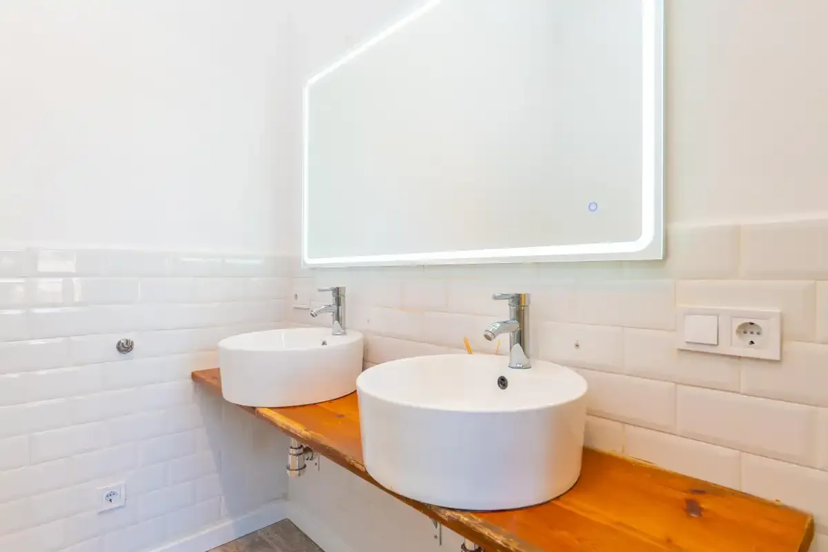 A bright bathroom with two white vessel sinks beneath a large mirror.