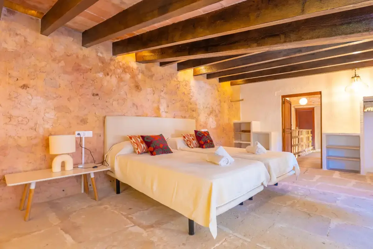 A bedroom with a large bed beneath exposed wooden ceiling beams.