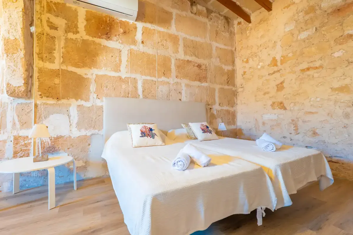 A bedroom with two beds, white bedding, and exposed stone walls.