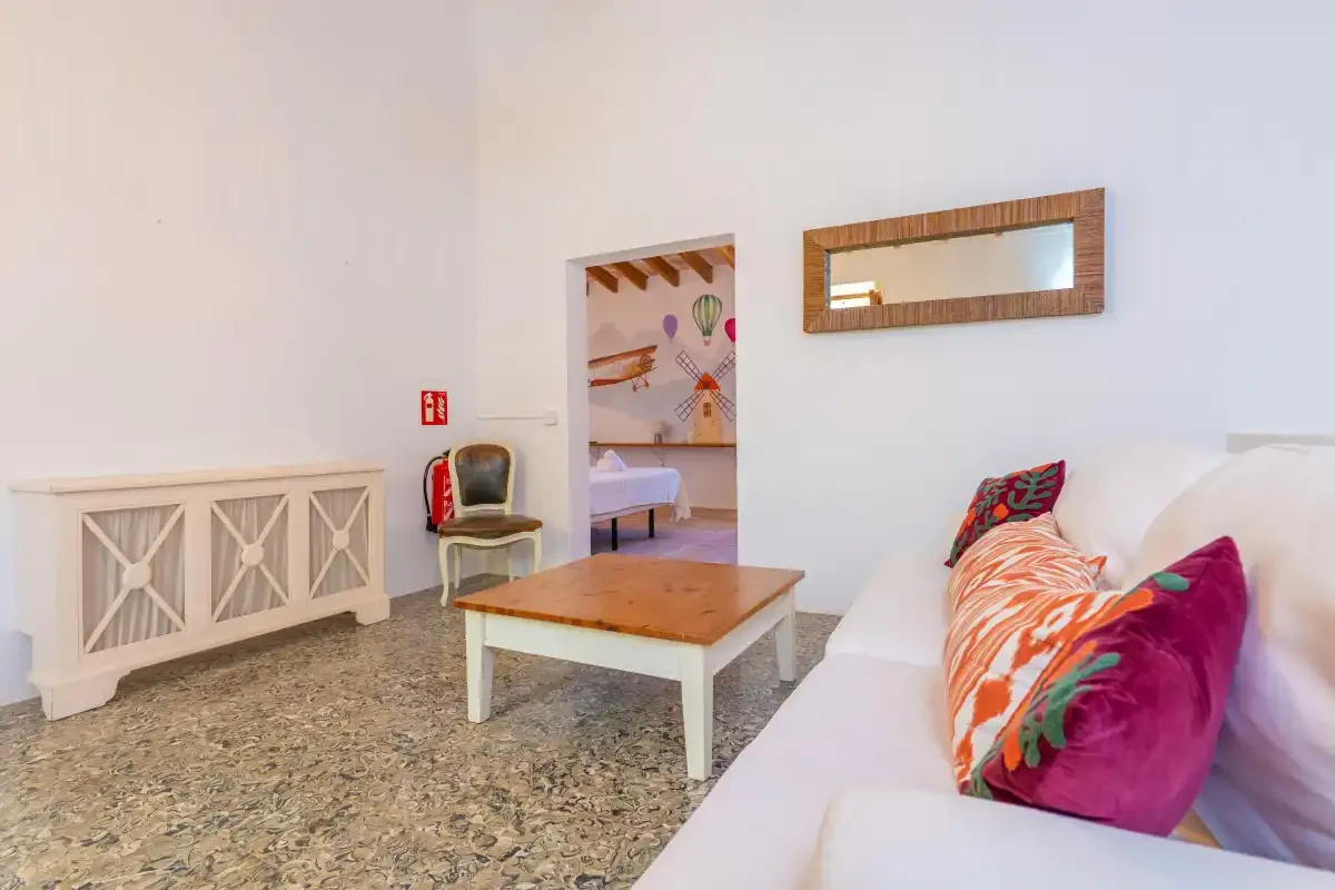 A living room with a white sofa, a wooden coffee table, and a wall mirror.
