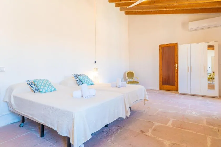 A bright bedroom with two beds and a wardrobe beneath exposed wooden ceiling beams.